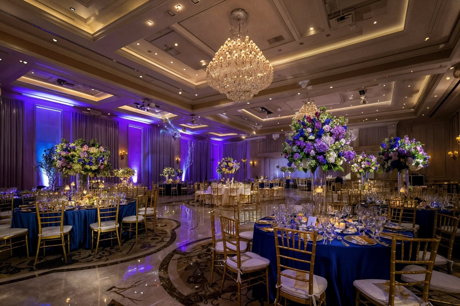 A Canadian wedding reception hall set with gold chairs, blue linens and tall floral centrepieces